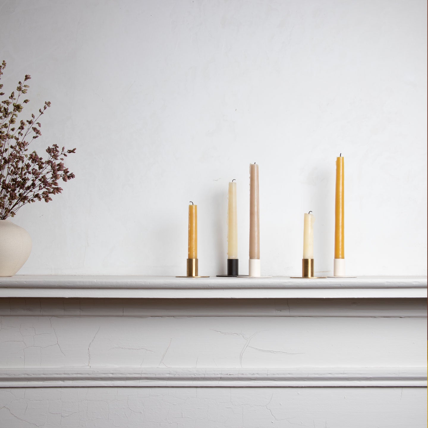 Group of taper candles in holders on a mantel.