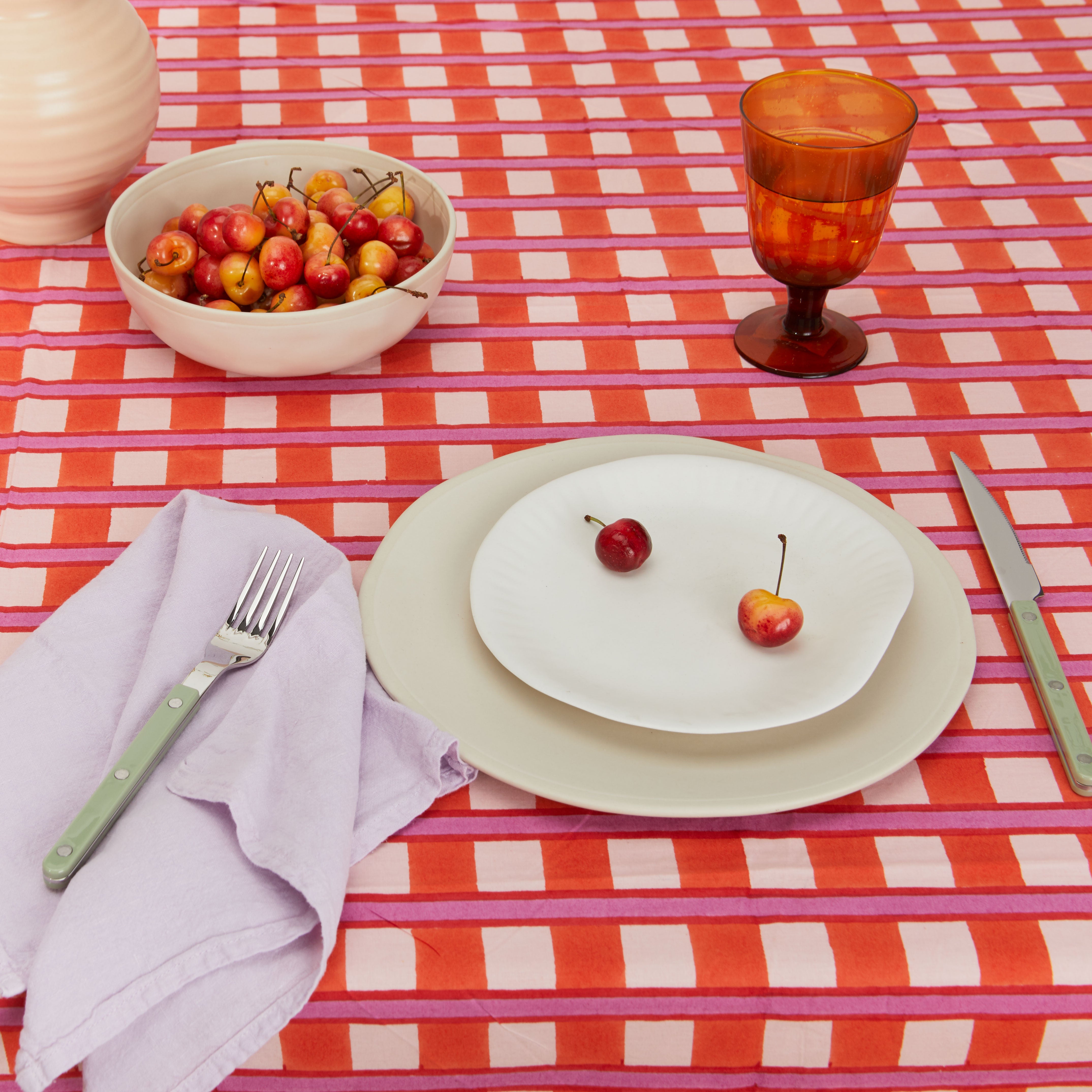 Picnic table setting with pitcher and blue glass tumblers on striped tablecloth.