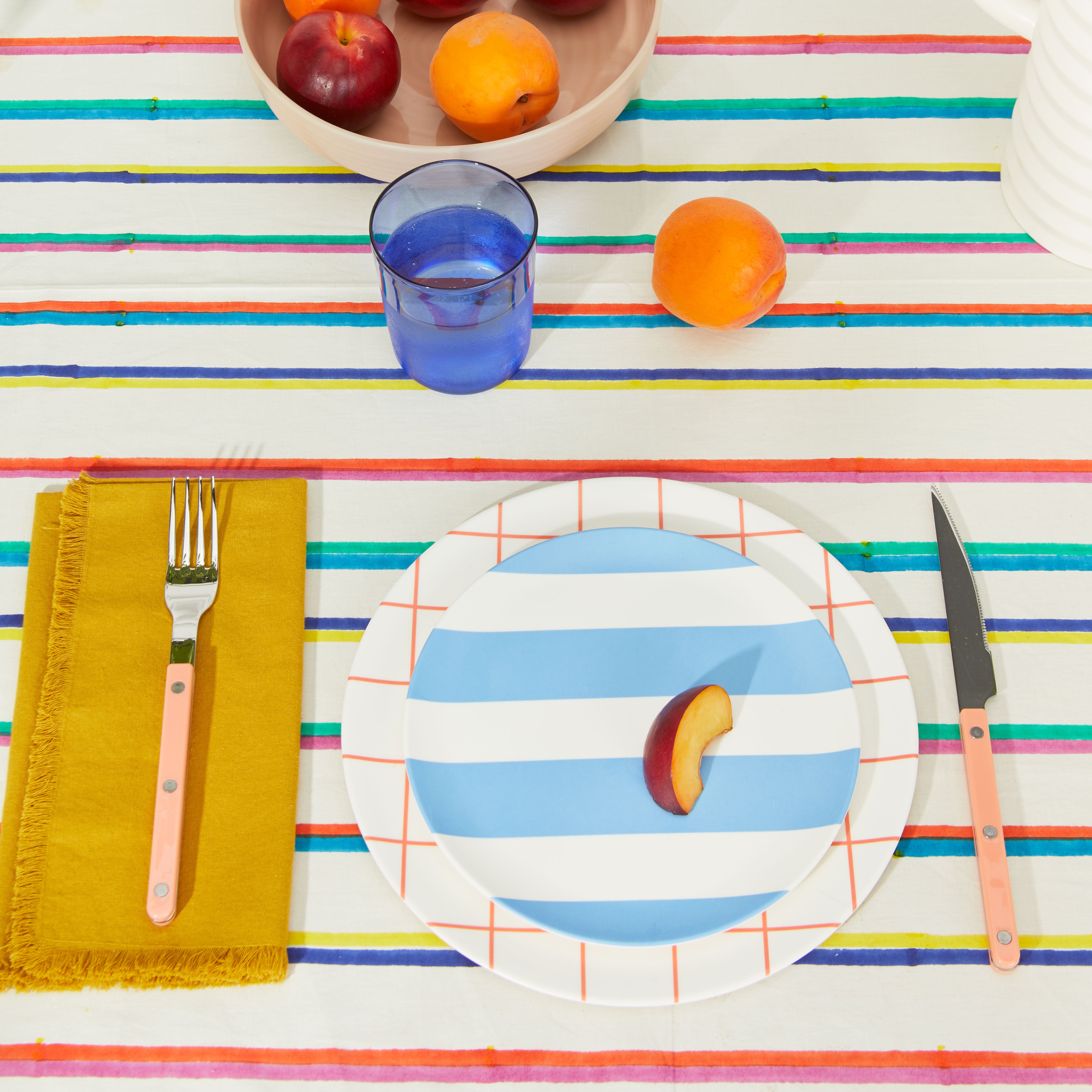 Place setting with blue glass tumbler on striped tablecloth.