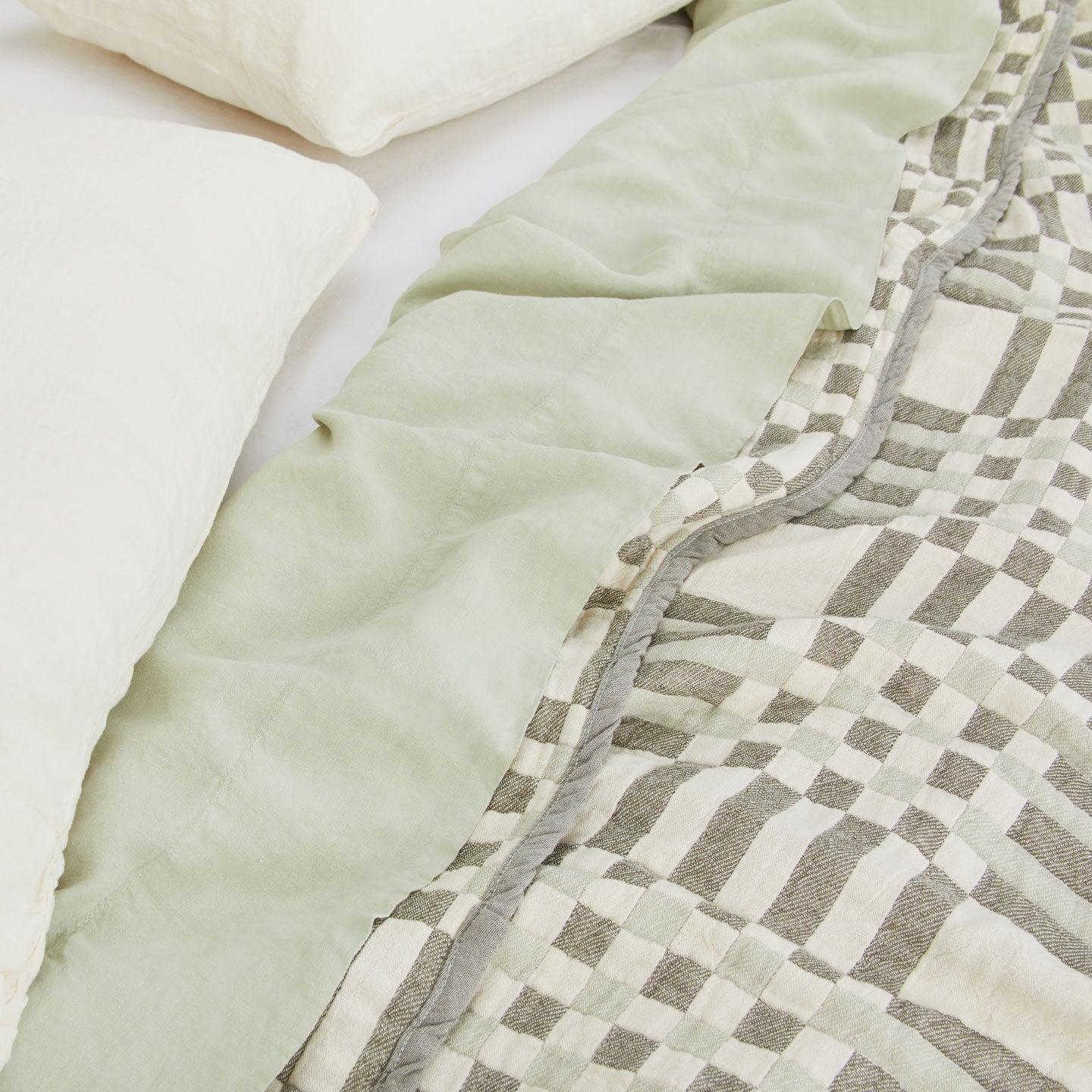 Simple Plaid Blanket in Olive and Sage on a bed with white, ivory, and sage pillows and sheets.