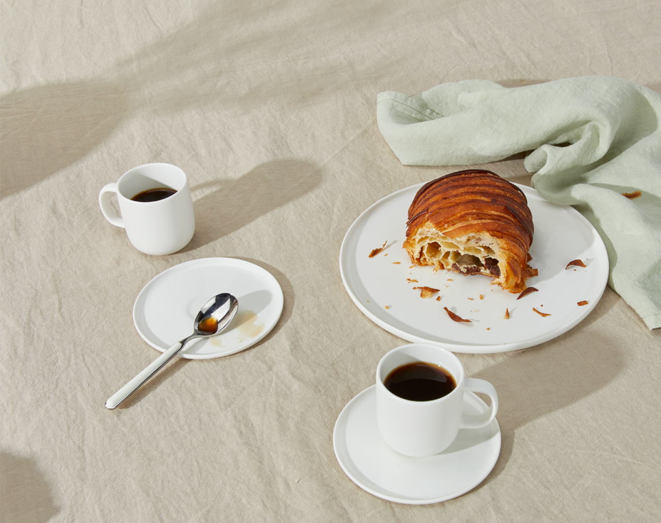 Simple Porcelain Espresso Mugs with spoon, pastry on Simple Porcelain Salad Plate, and Simple Linen Napkin in Sage.