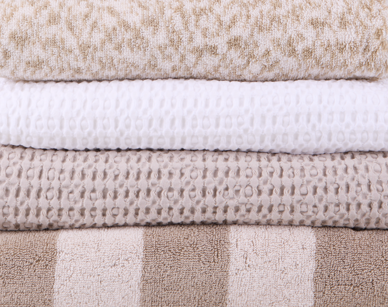 A stack of neutral colored towels in various patterns and textures.