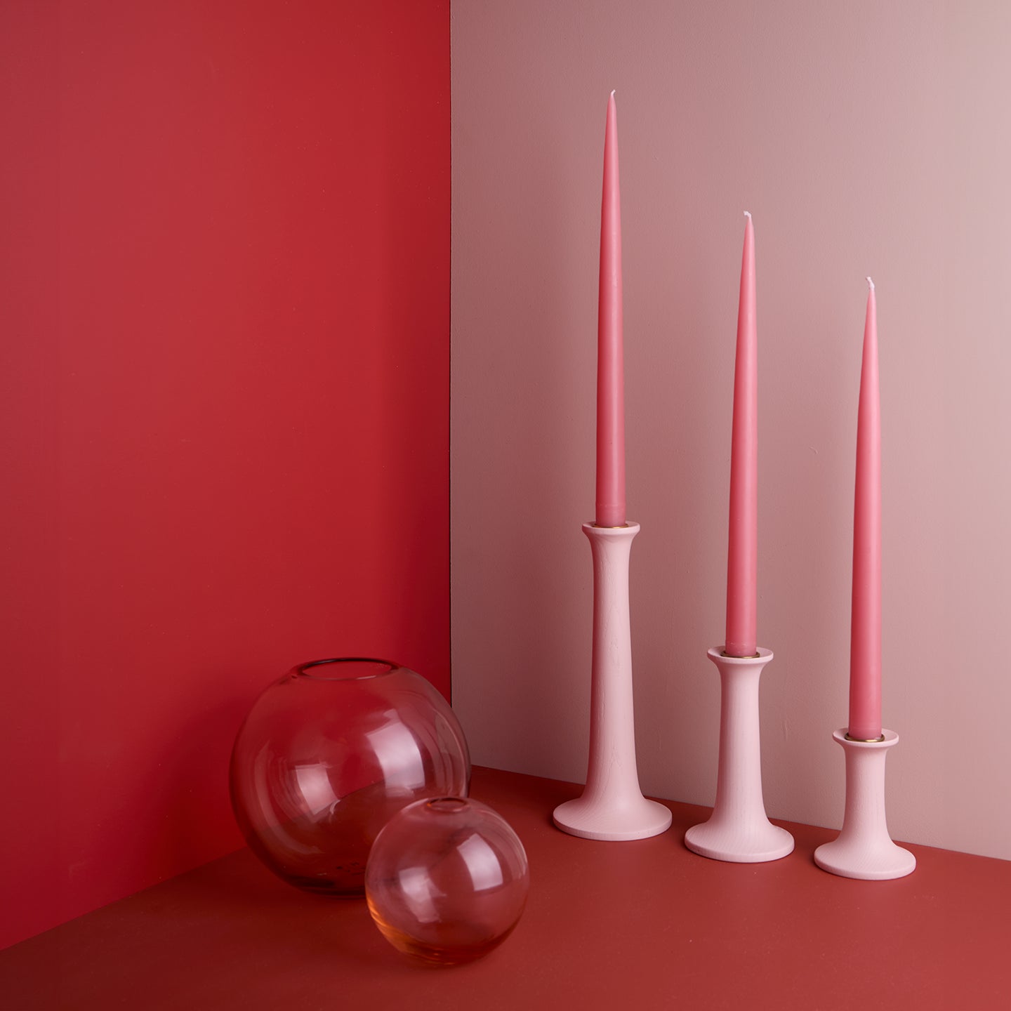 A pair of glass sphere vases and a trio of taper candle holders with taper candles. All in Blush tones.