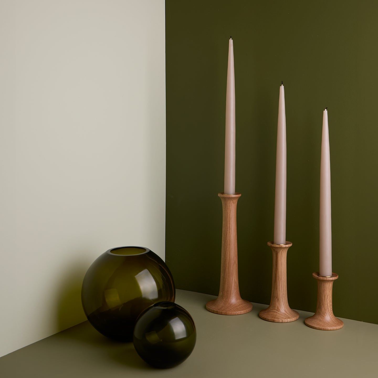 A pair of glass sphere vases and a trio of taper candle holders with taper candles. All in Olive tones.