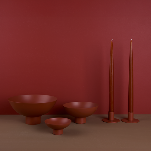 A trio of footed bowls and pair of candle holders, all in Terracotta, with red-orange taper candles.