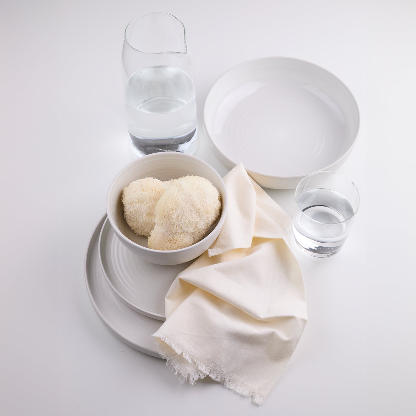 Essential dinnerware, glassware, pitcher, and napkins in light neutral tones.