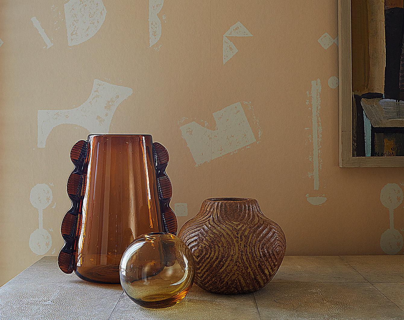 A grouping of vases on a dresser top against a patterned wallpaper background.