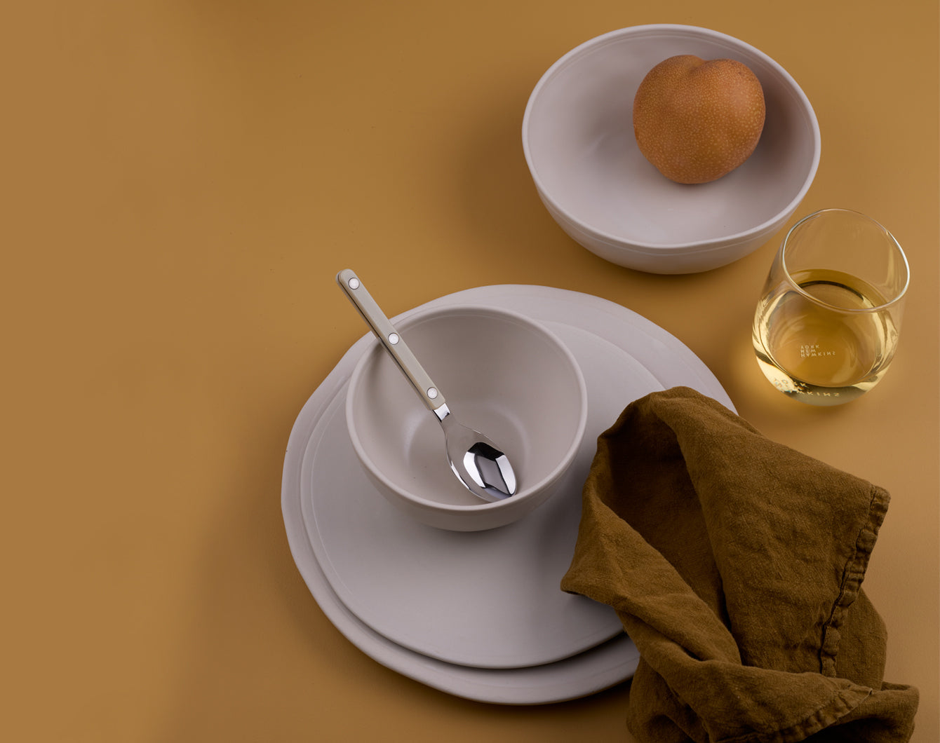 An arrangement of dinnerware with linen napkin and wine glass on ochre background.