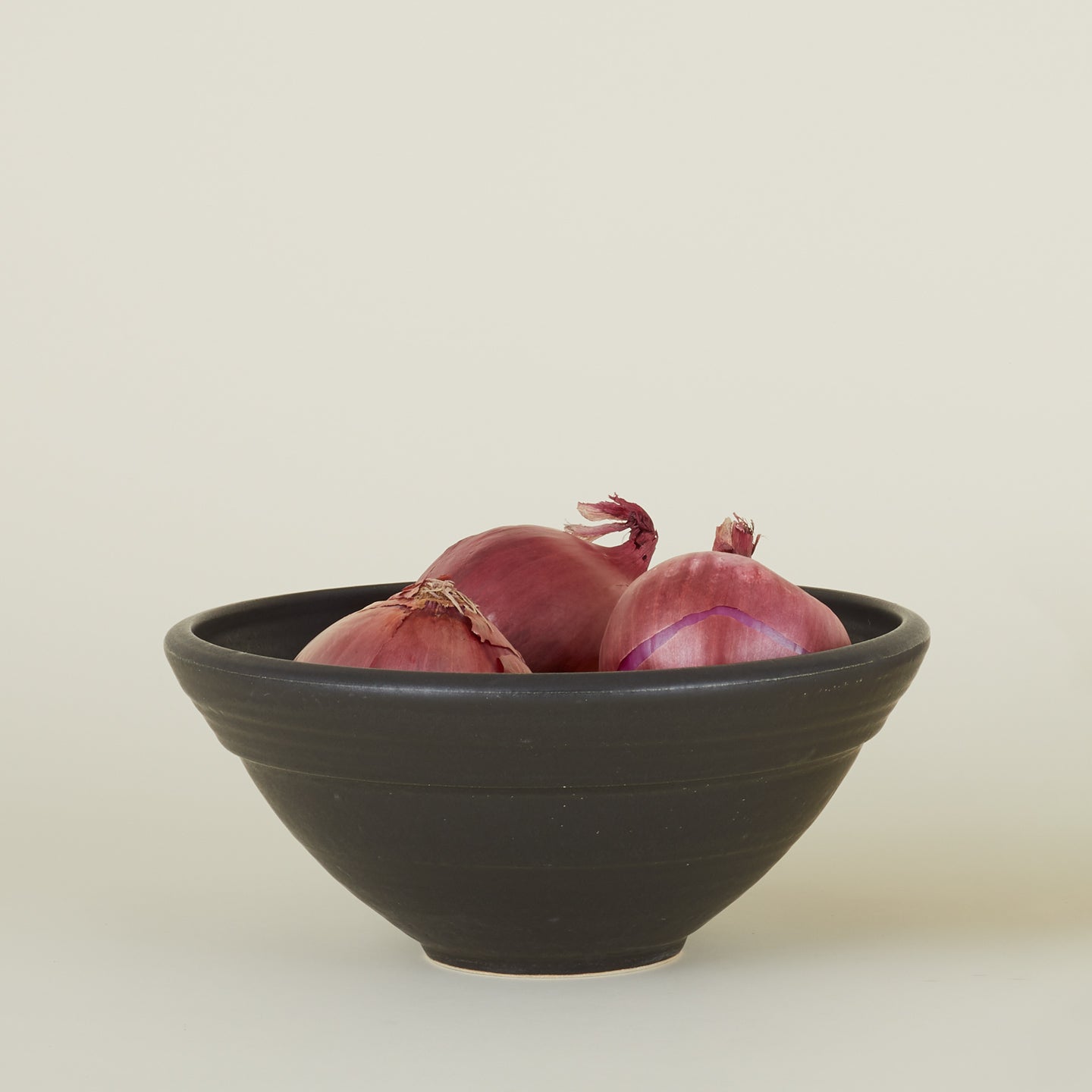 Stoneware Serving Bowl in Black, filled with red onions.