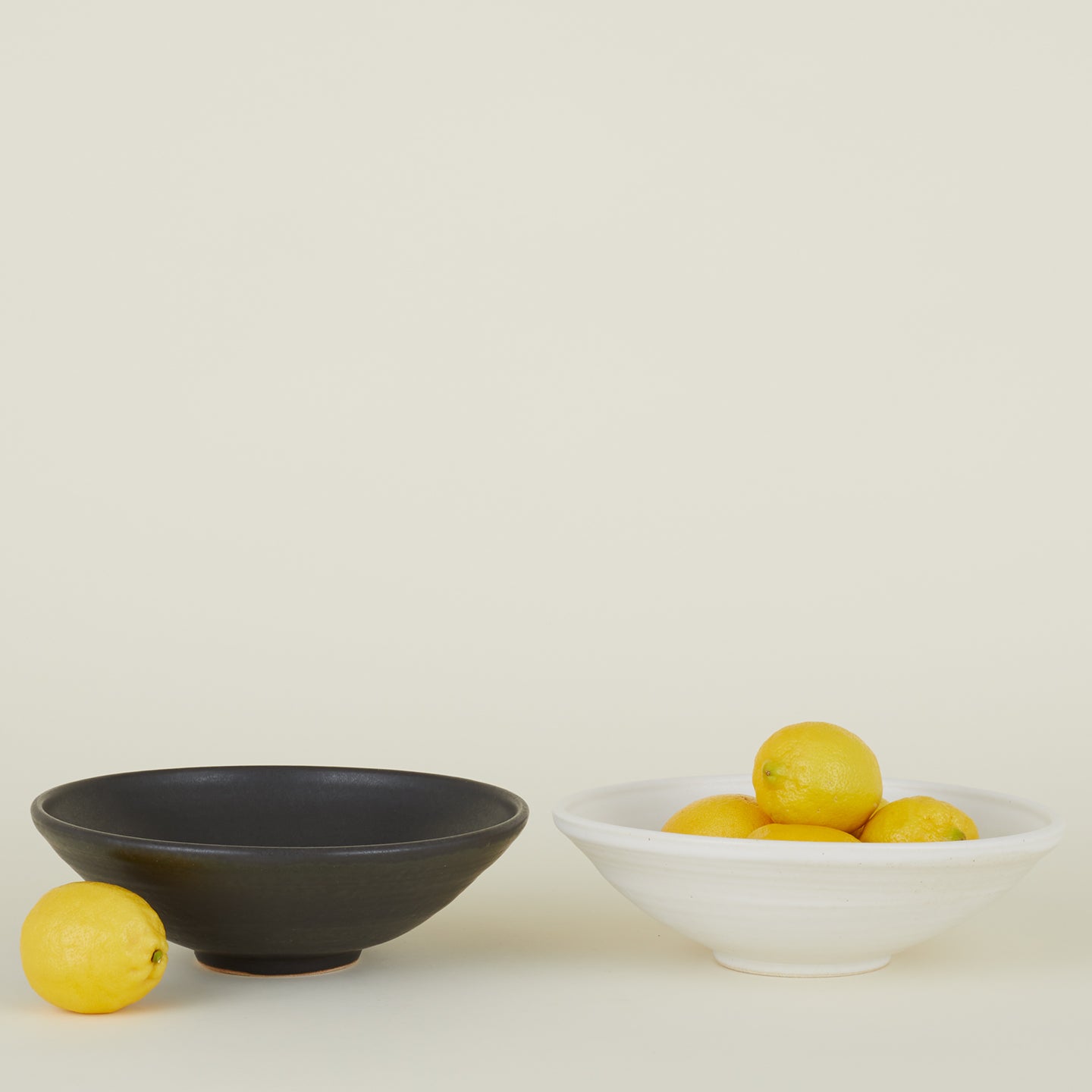 Two Stoneware Flared Bowls, one in Black and one in Eggshell, filled with lemons.
