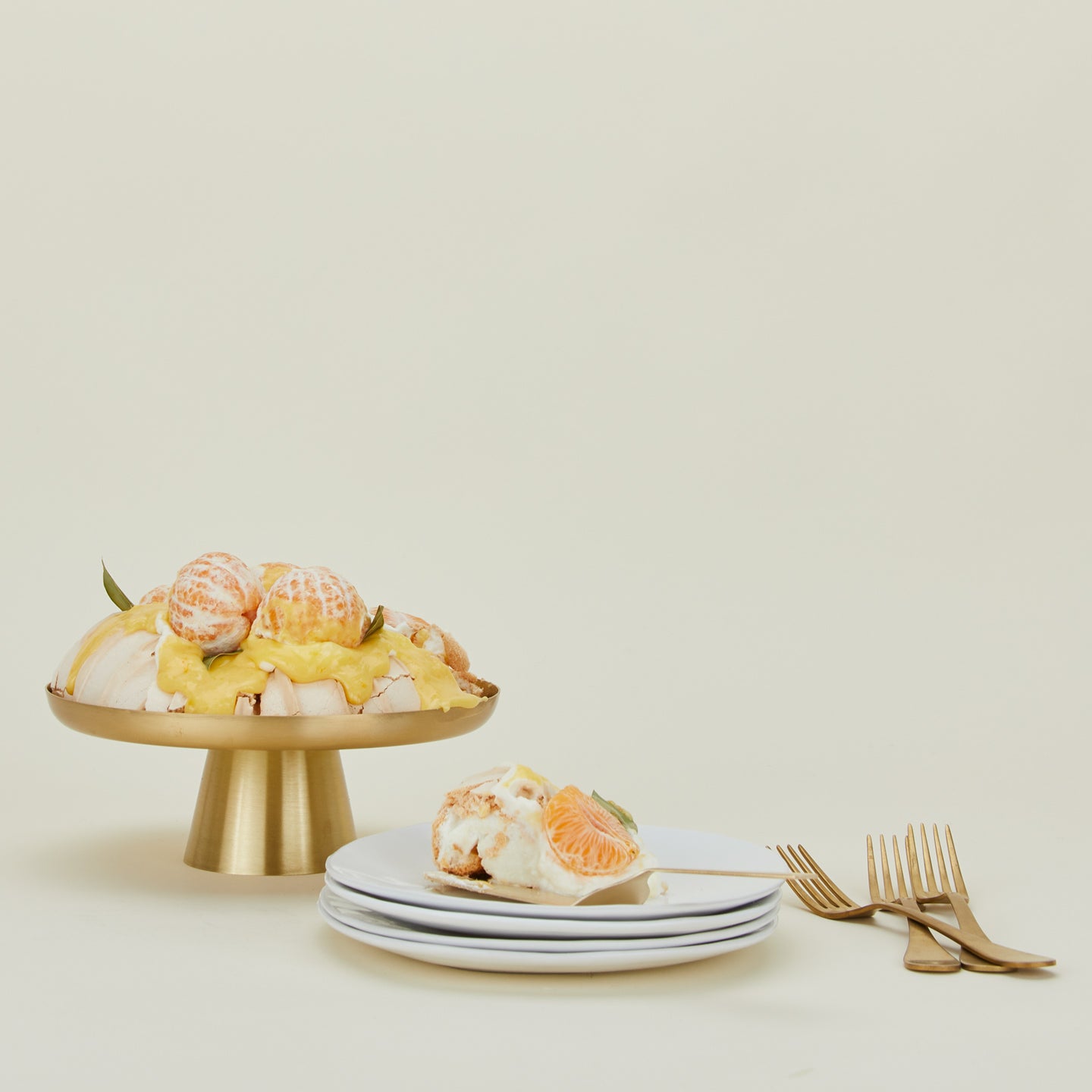 Brass Cake Stand with pavlova, stack of plates and bunch of forks.