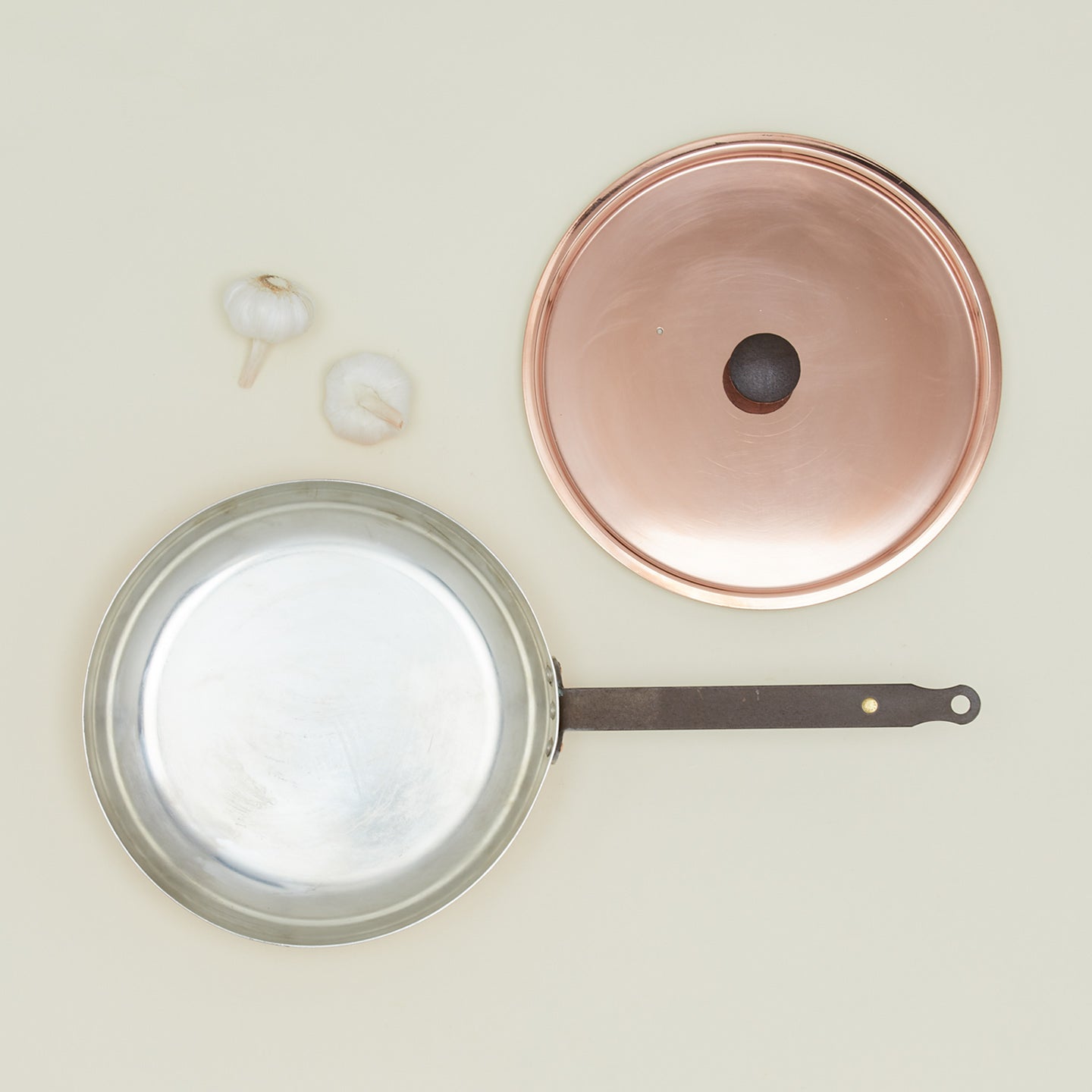 Overhead of copper frying pan with lid and cloves of garlic