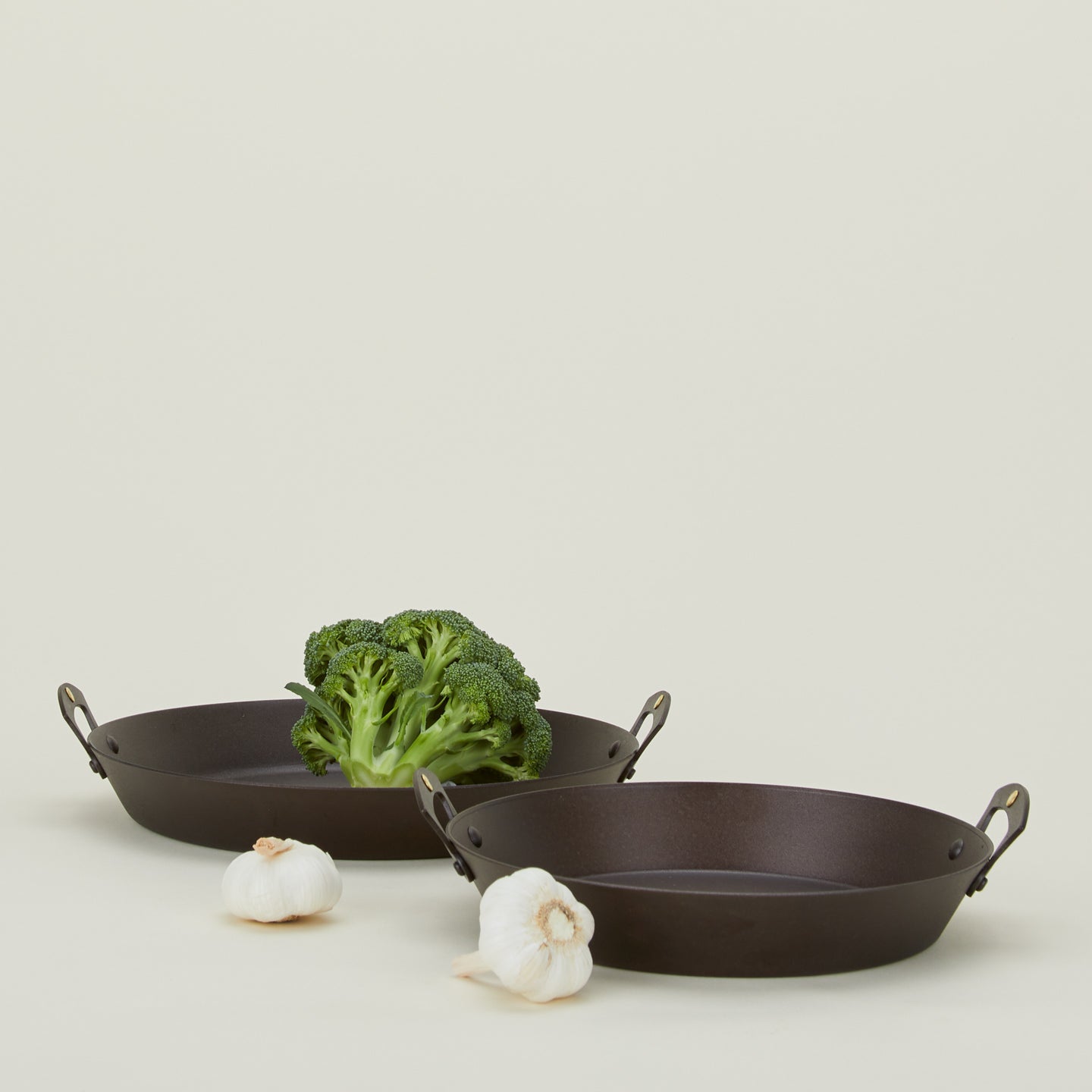 Large and small spun iron two handled saute pans with garlic and broccoli 