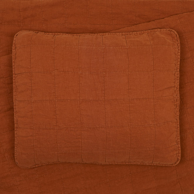 A rectangular quilted orange pillow sits on an orange quilted bedspread.