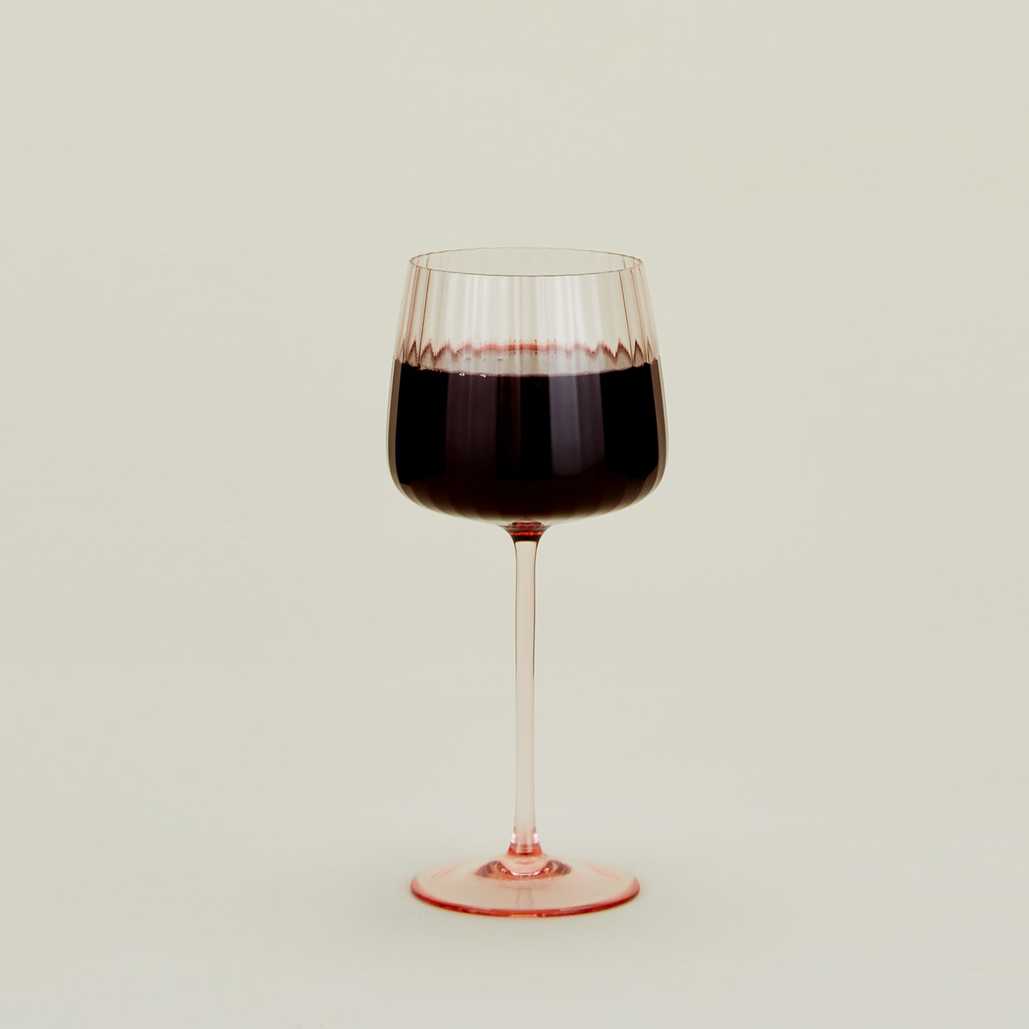 Pink ribbed red wine glass filled with red wine.
