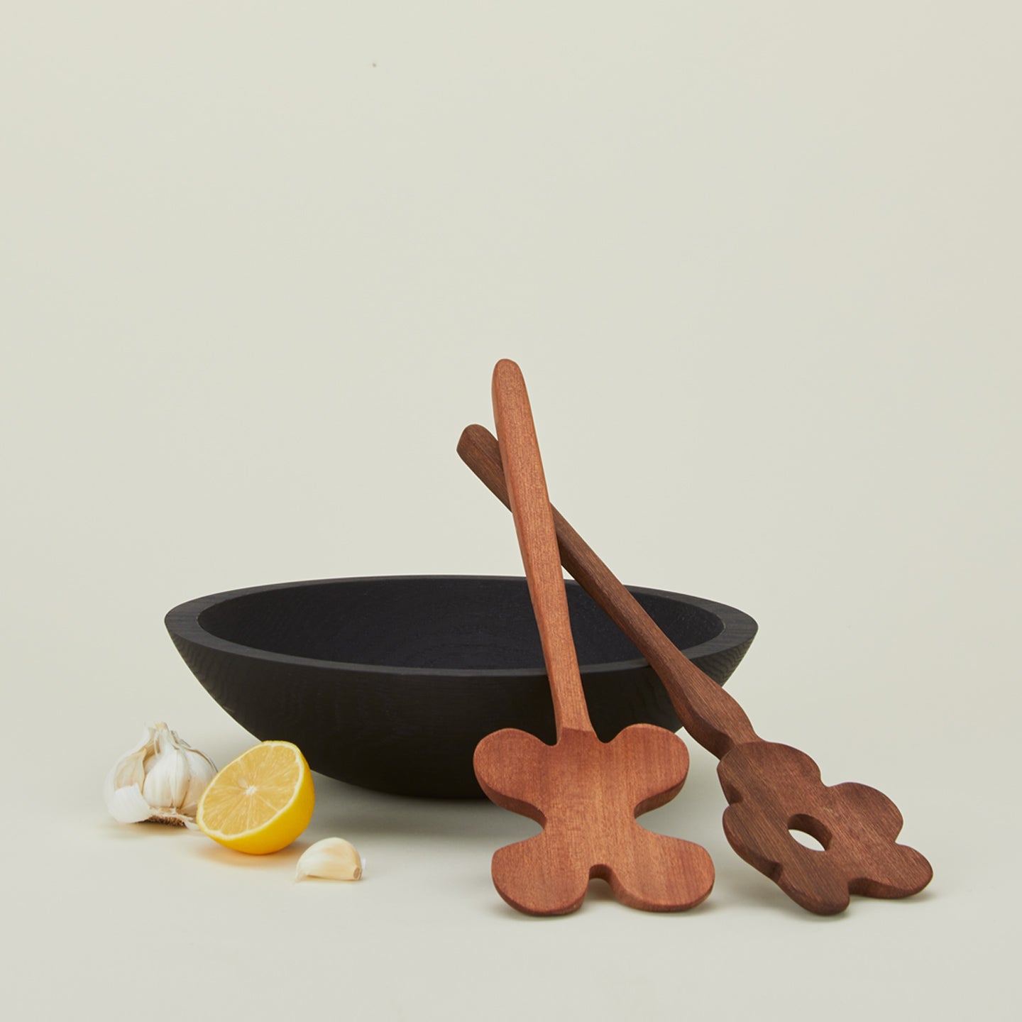 Walnut Areaware floral salad servers propped up against a wooden bowl with a lemon and garlic