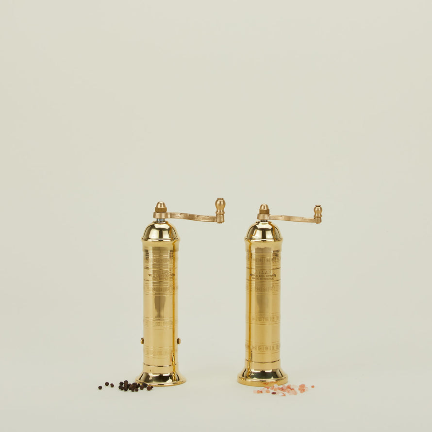 A pair of brass salt and pepper mills with peppercorns and coarse salt.