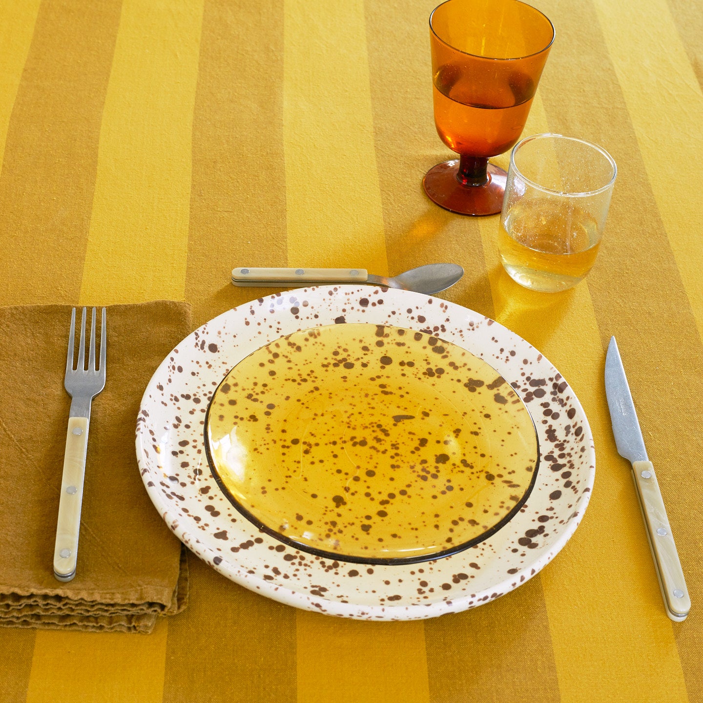 Placesetting with Glass Salad Plate in Amber on yellow striped tablecloth.