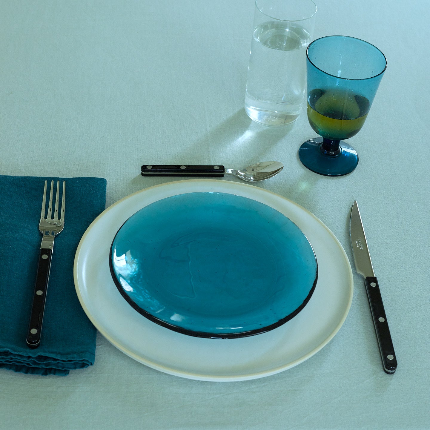 Placesetting with Glass Salad Plate in Peacock on yellow striped tablecloth.