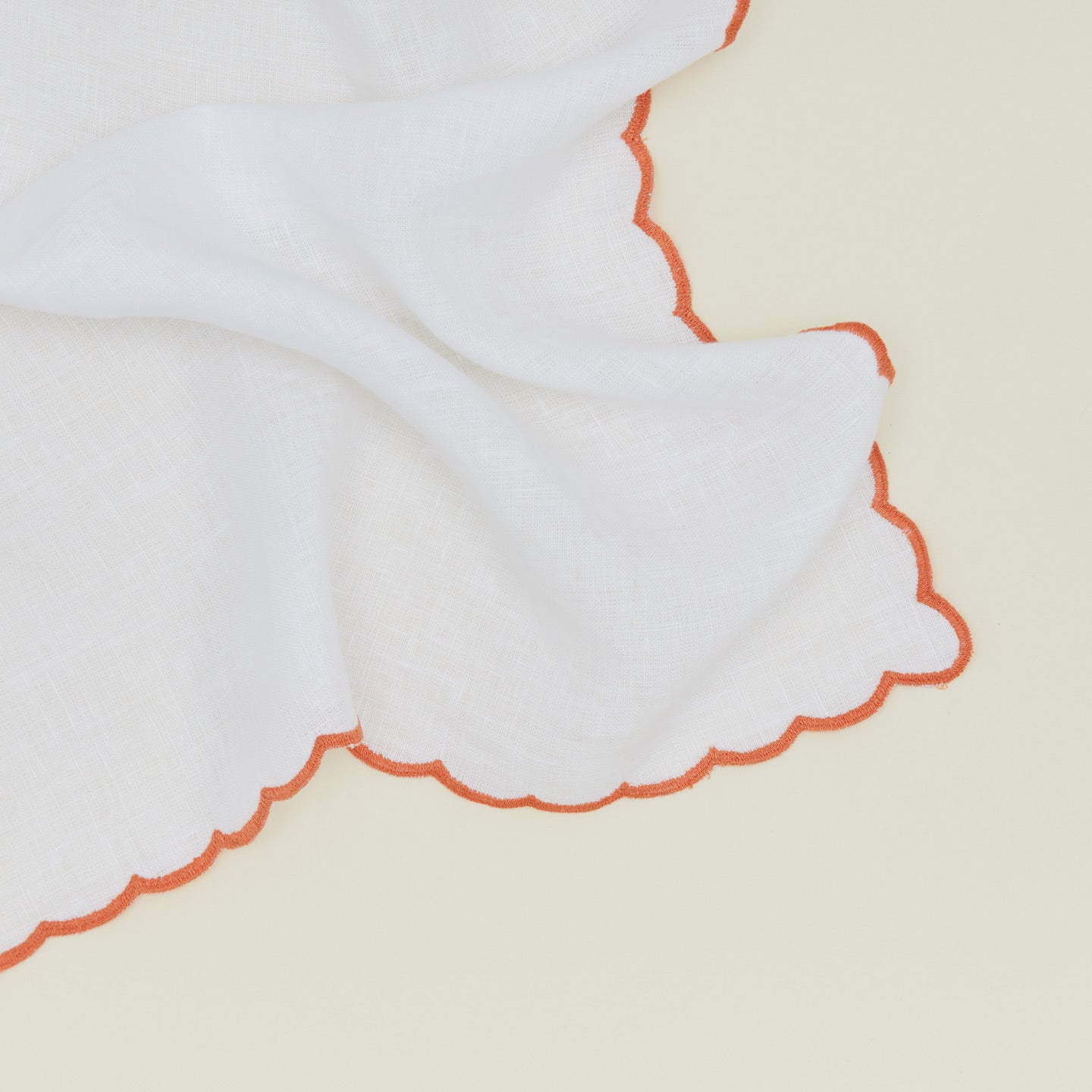 Detail of a napkin with a scalloped edge in orange.