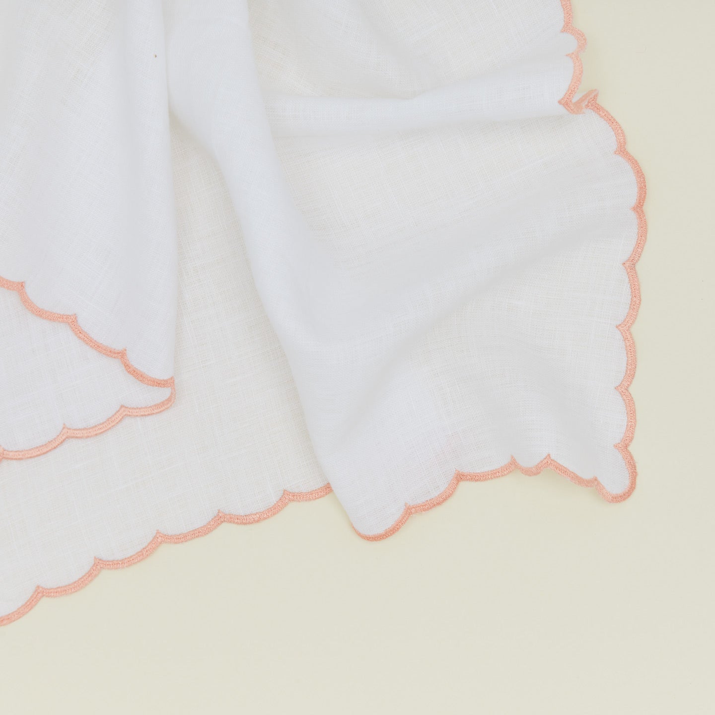 Detail of a napkin with a scalloped edge in pink.