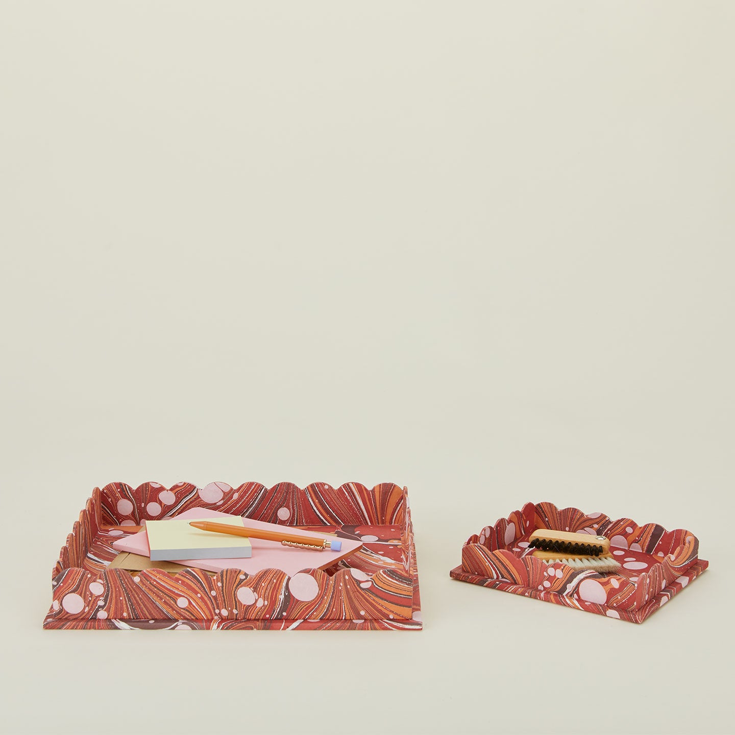 Set of two scalloped marbled trays in red with office supplies.