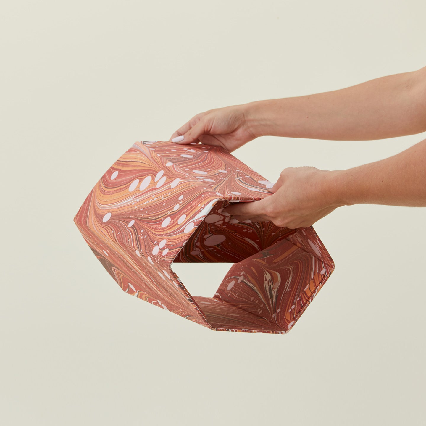 Hands unfolding collapsible marbled scalloped wastebasket.