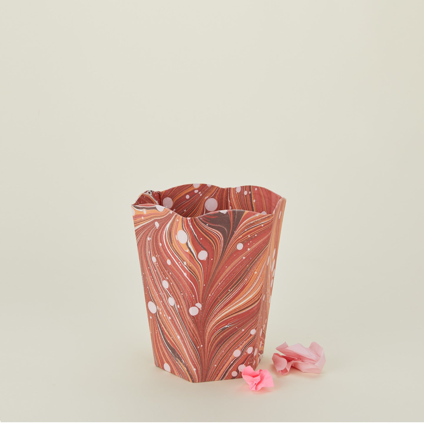 Marbled scalloped wastebasket in red with balled-up paper.