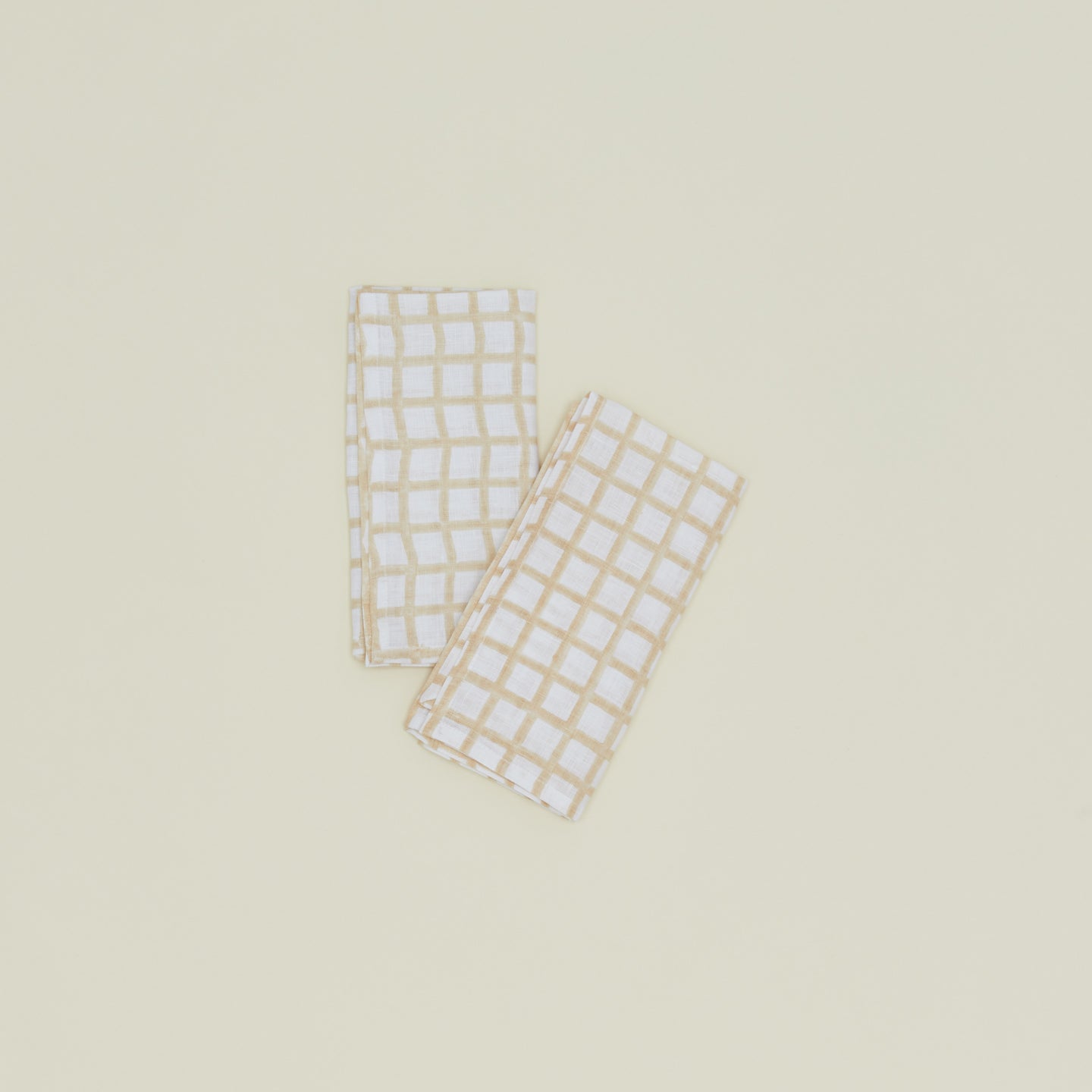 A set of two block printed napkins with a grid pattern in tan.