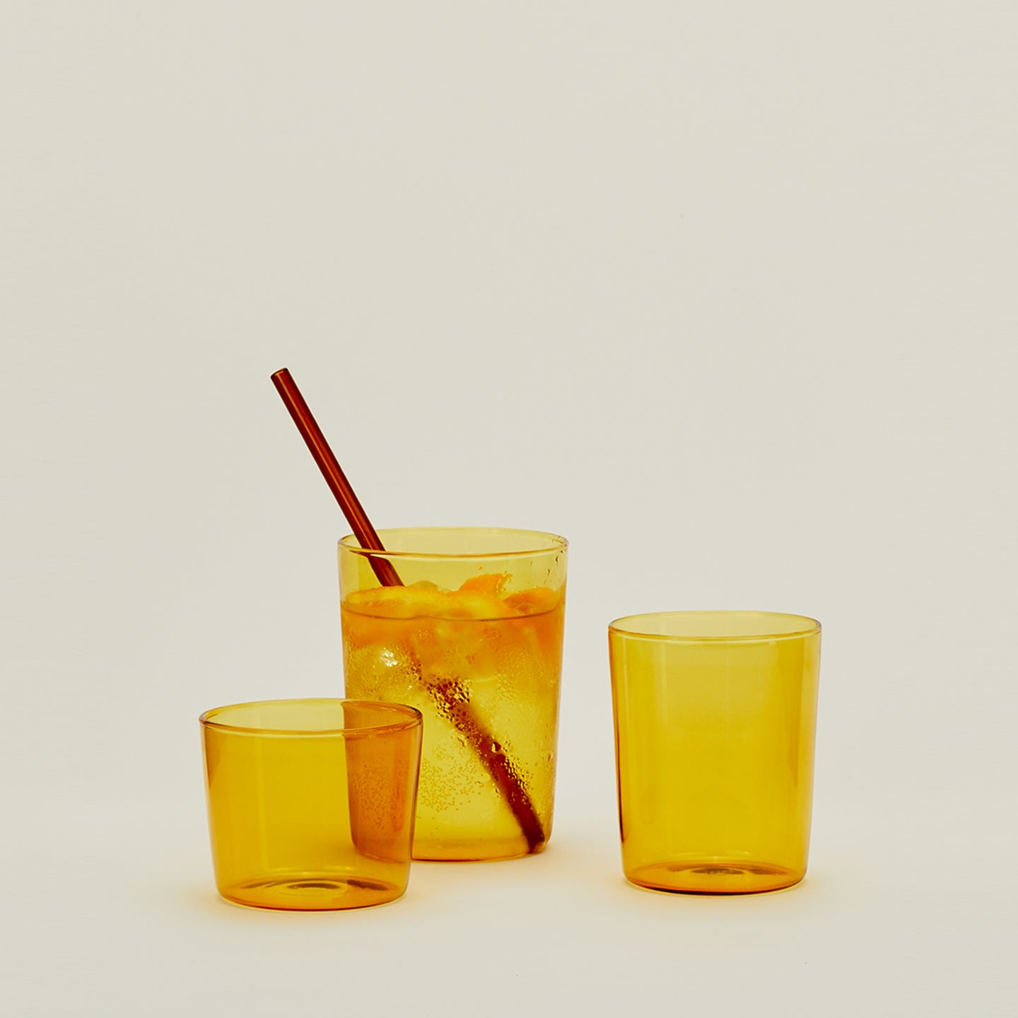 Group of three Essential Glasses in Amber in various sizes, filled with water and fruit with a coordinating glass straw.