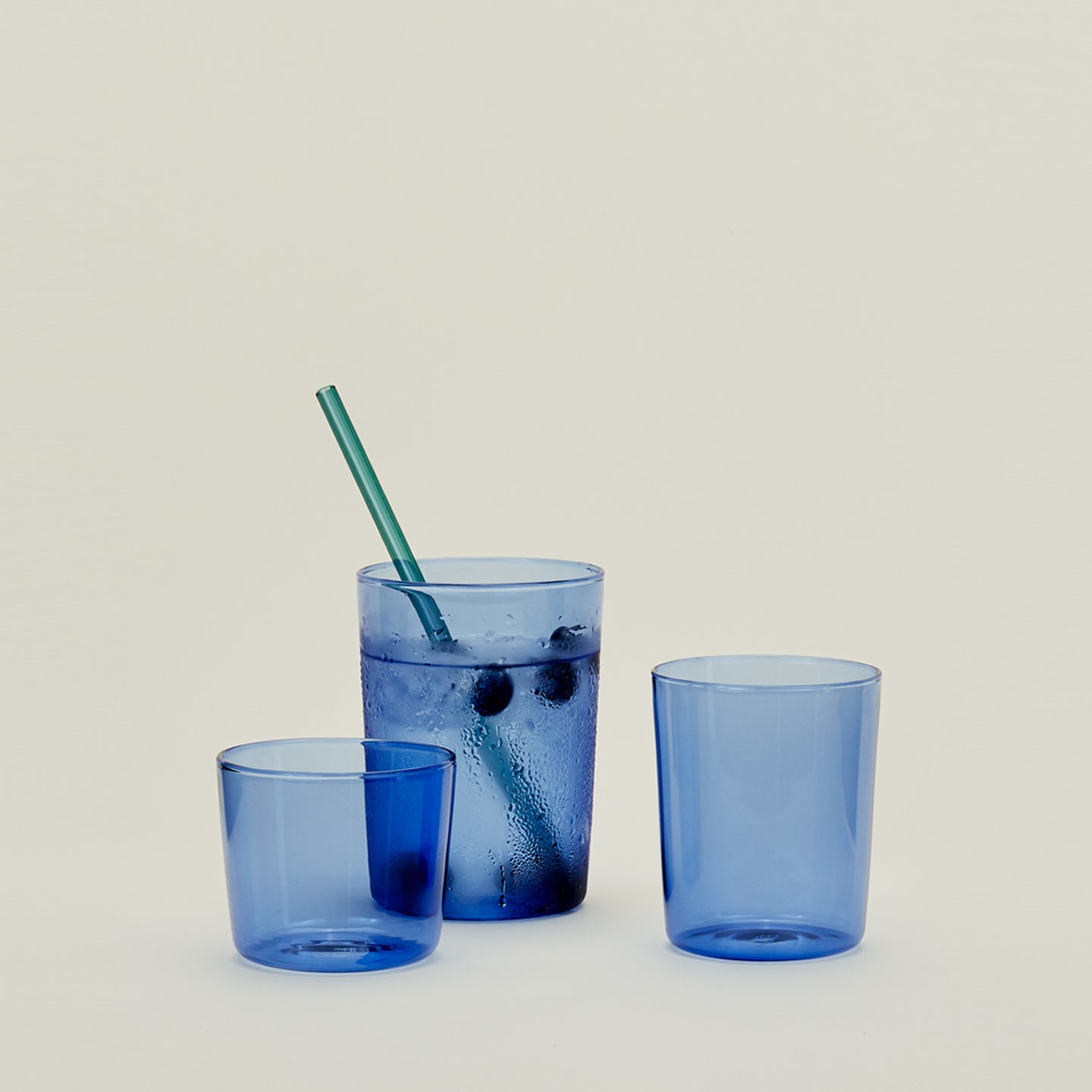 Group of three Essential Glasses in Blue in various sizes, filled with water and fruit with a coordinating glass straw.