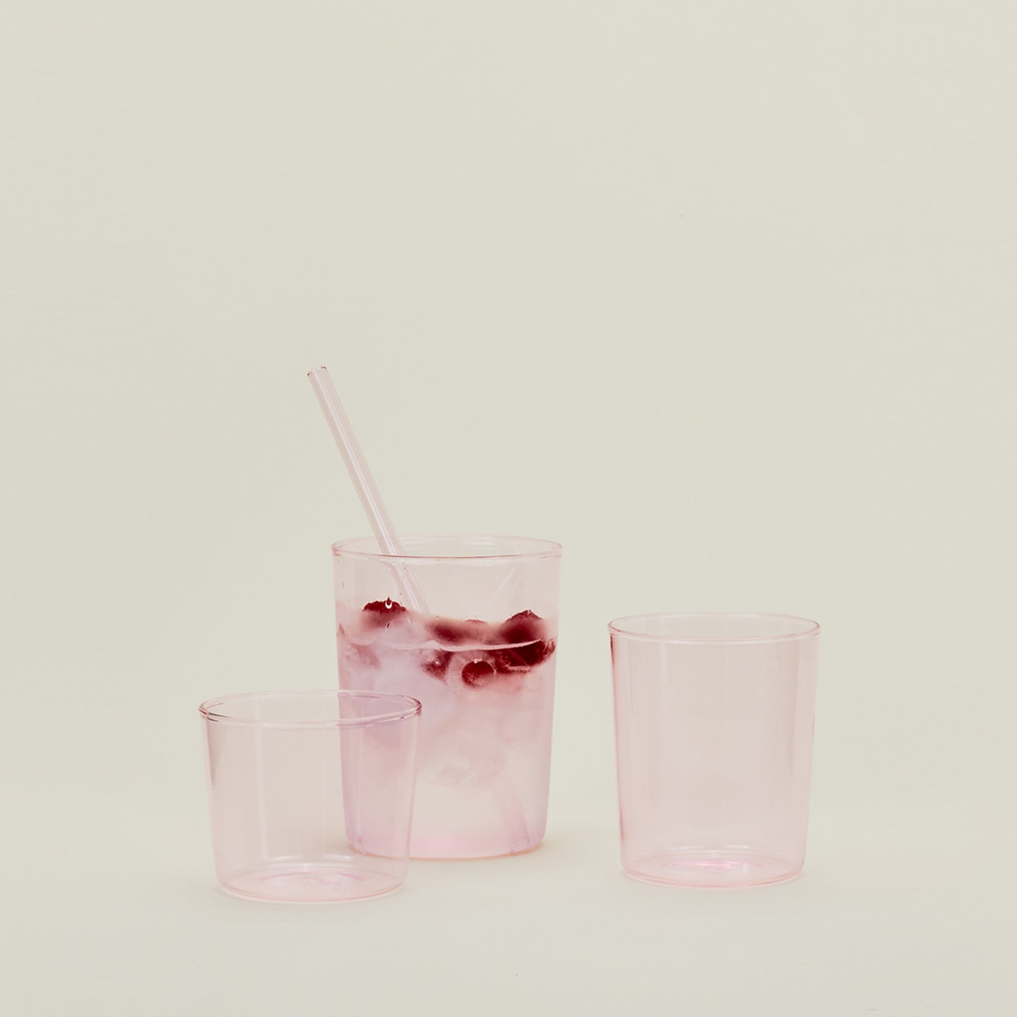 Group of three Essential Glasses in Blush in various sizes, filled with water and fruit with a coordinating glass straw.