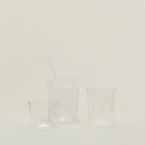 Group of three Essential Glasses in Clear in various sizes, filled with water and fruit with a coordinating glass straw.