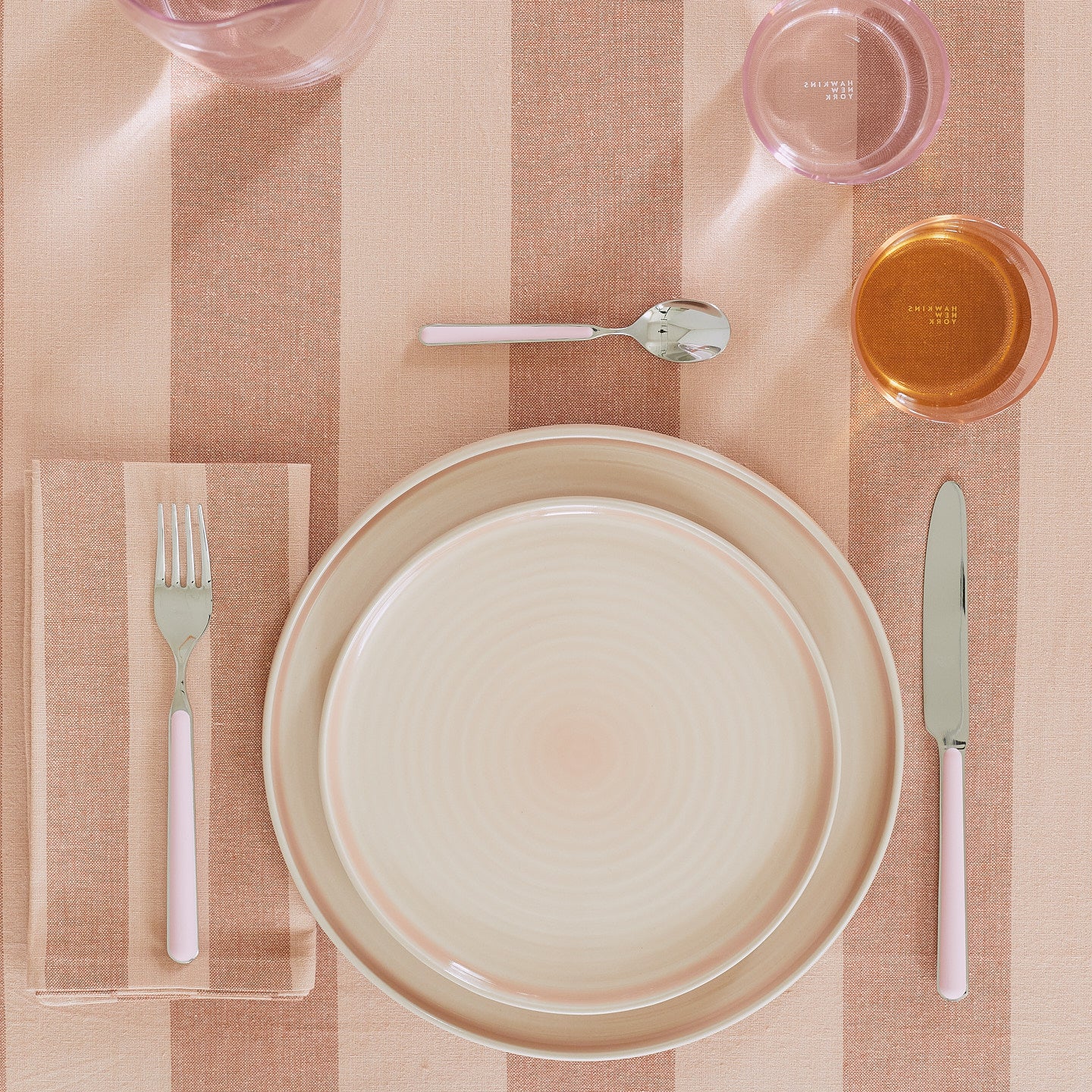 Placesetting with Essential Dinner Plate in Blush on pink striped tablecloth.