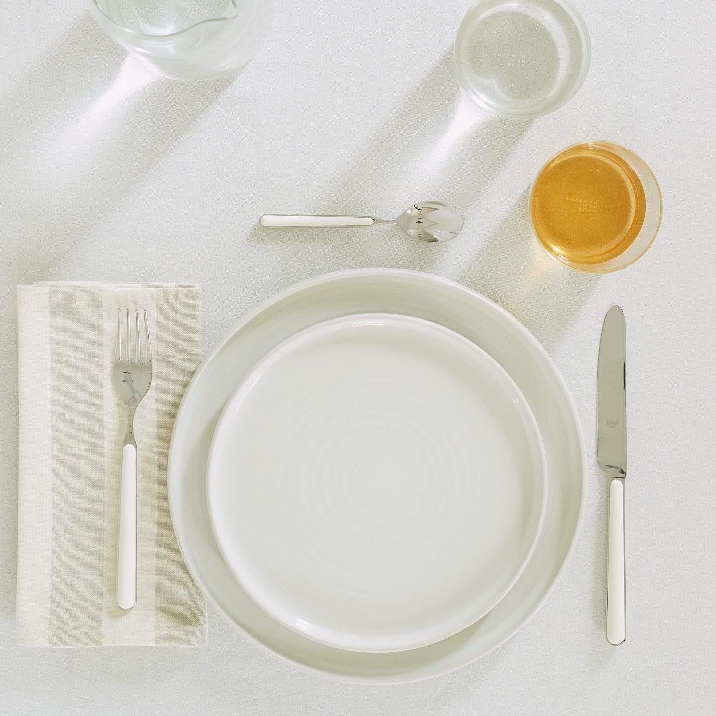 Placesetting of bone white Essential dinnerware on white tablecloth.