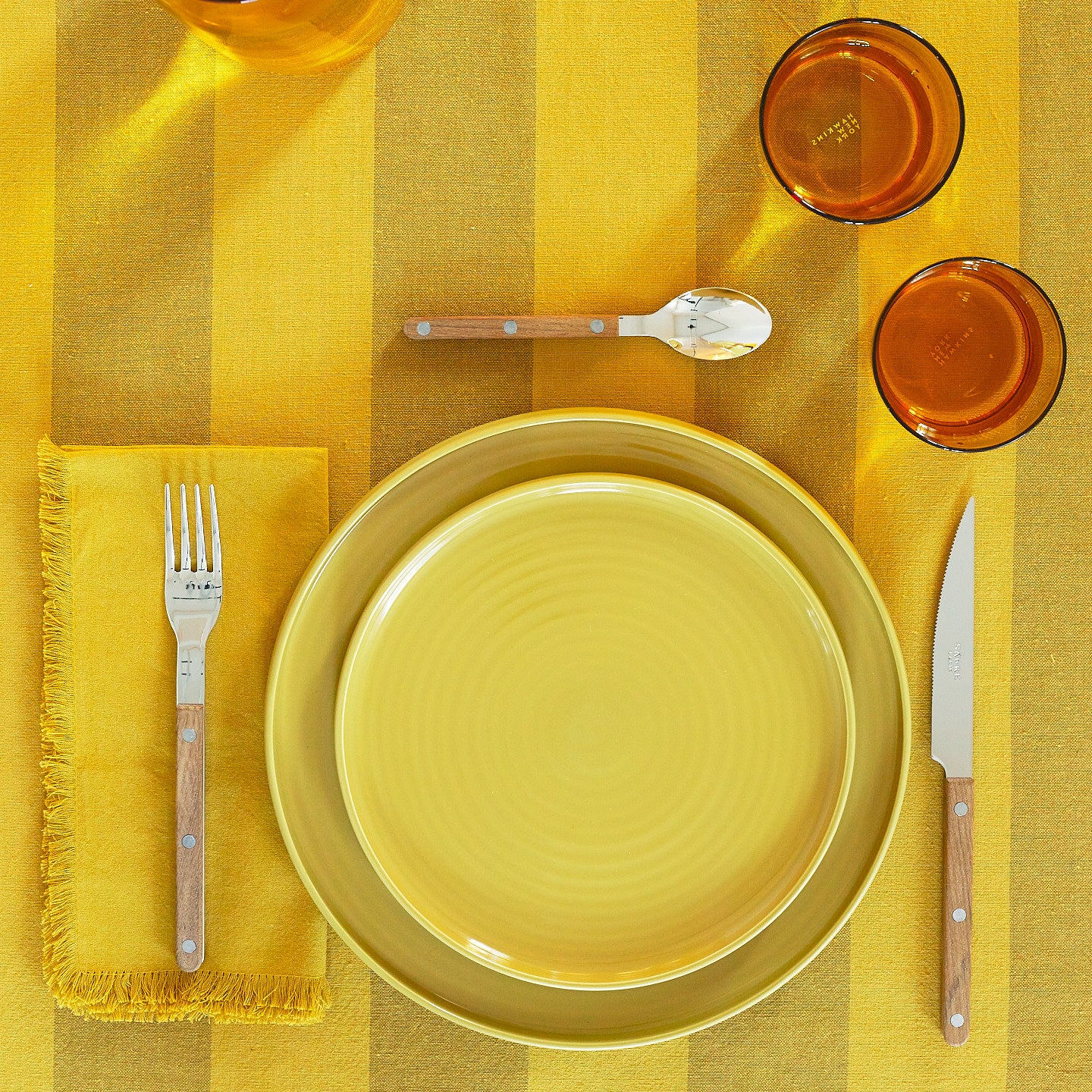 Placesetting with Essential Salad Plate in Mustard on yellow striped tablecloth.