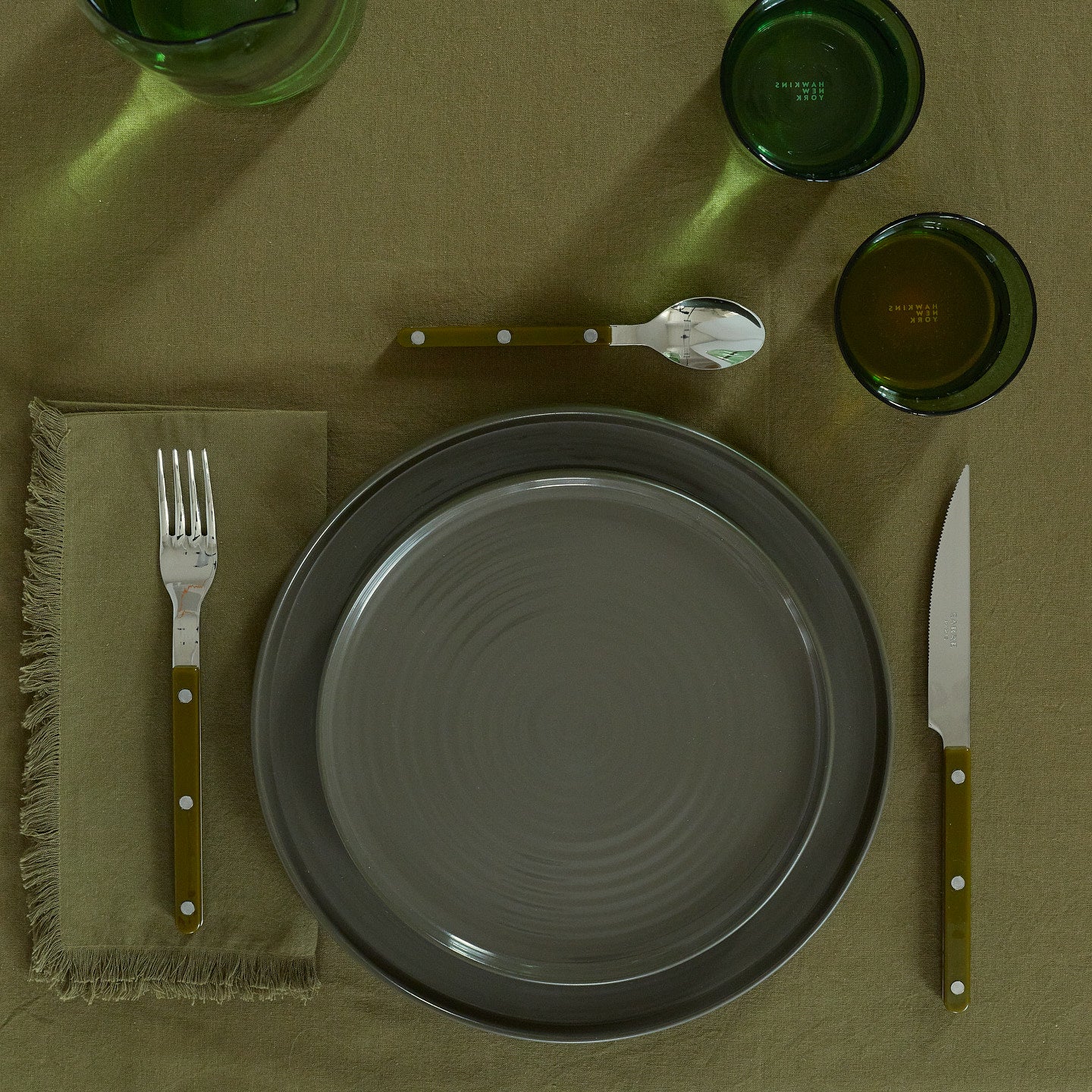 Placesetting with Essential Dinner Plate in Olive on green tablecloth.