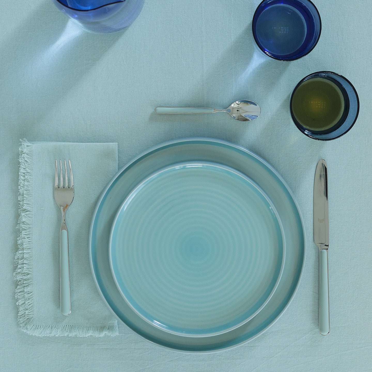 Placesetting of sky blue Essential dinnerware on blue tablecloth.