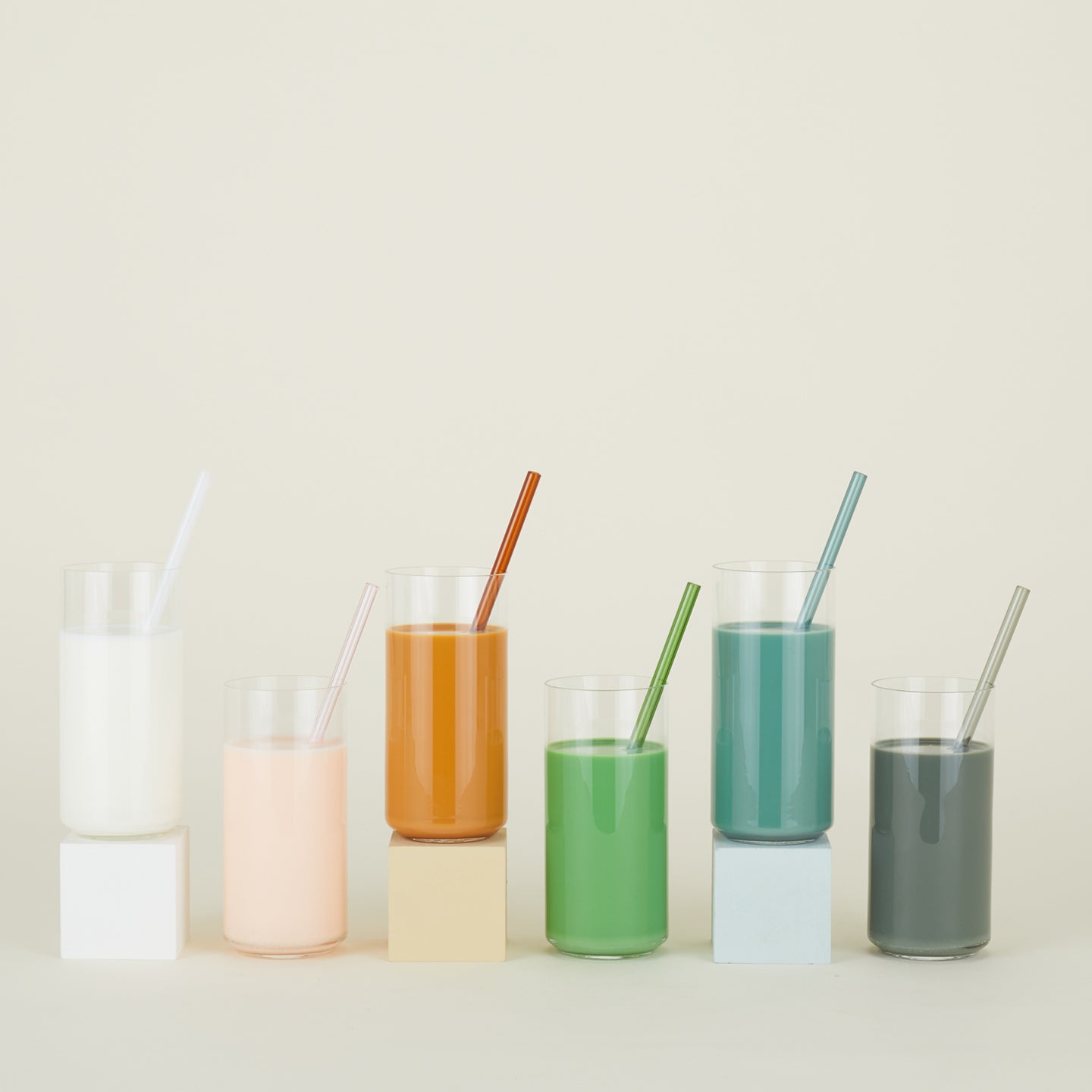 Row of drinking glasses filled with various colorful liquids, each with an Essential Glass Straw.