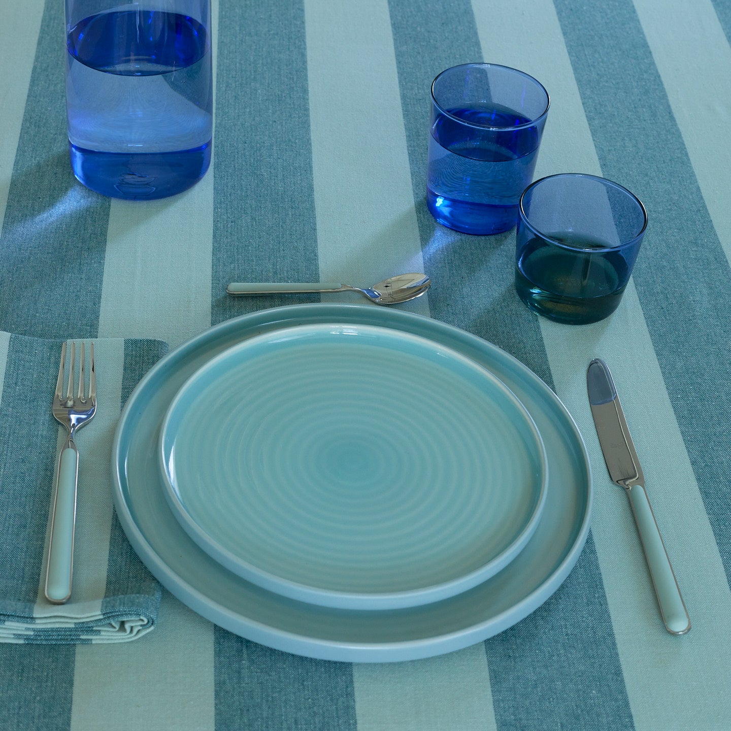 Placesetting with Essential Glassware in Blue on blue striped tablecloth.