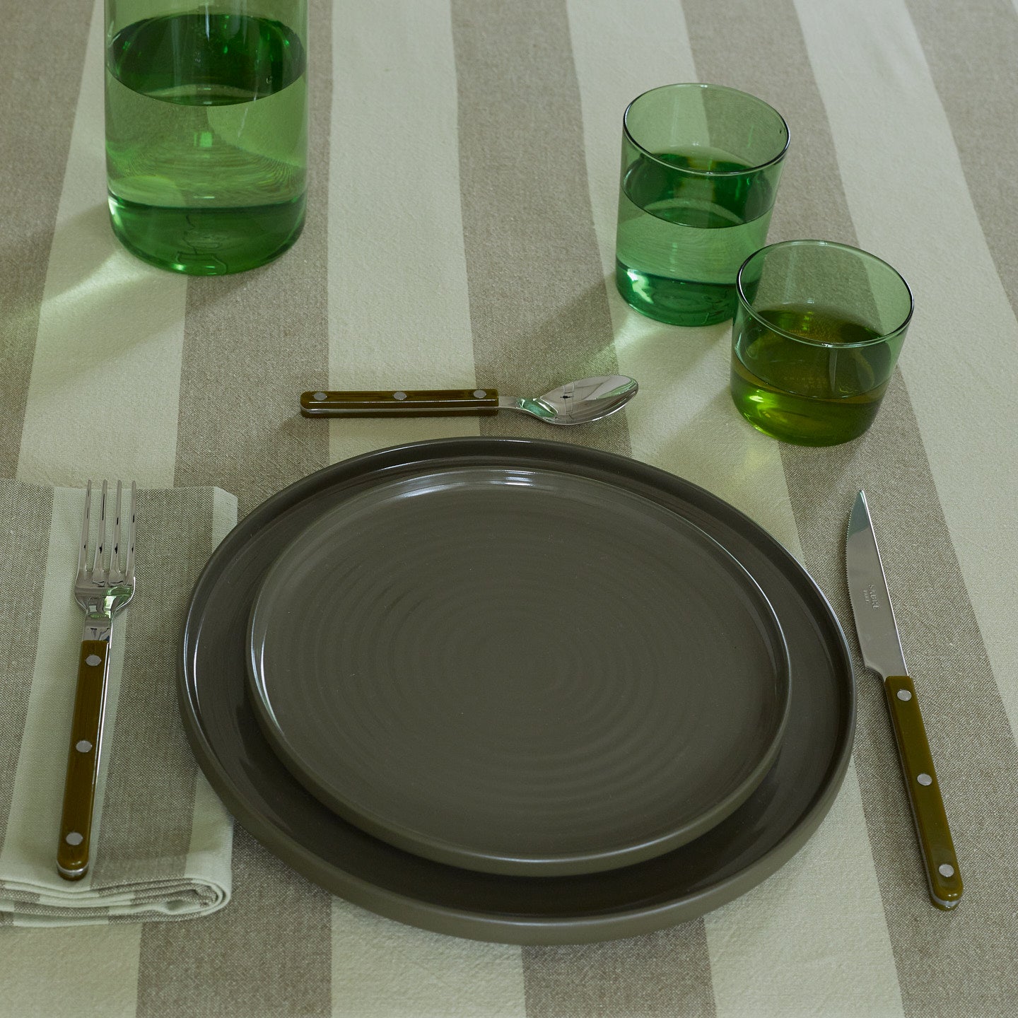 Placesetting with Essential Glassware in Green on green striped tablecloth.