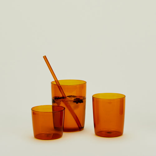 Group of three Essential Glasses in Terracotta in various sizes, filled with water and fruit with a coordinating glass straw.