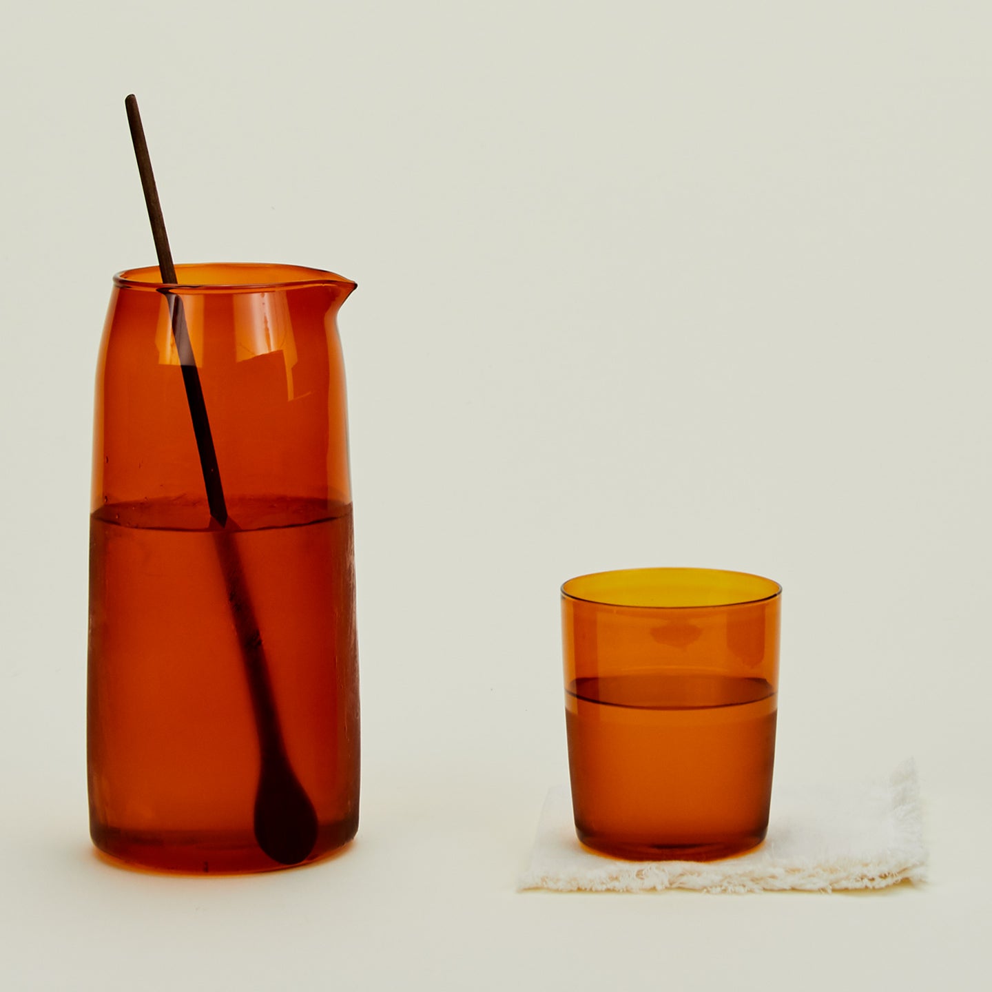 Essential Glassware Pitcher in Terracotta, filled with ice water, along with a drinking glass and stirring spoon.