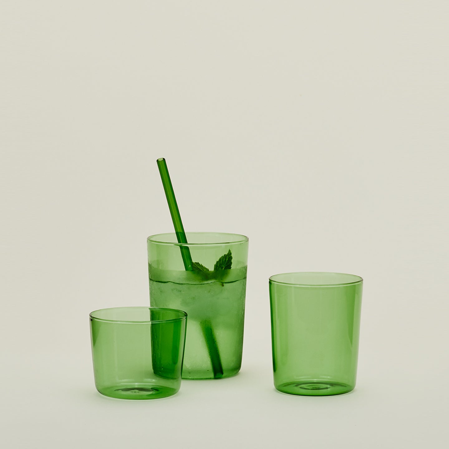 Group of three Essential Glasses in Green in various sizes, filled with water and fruit with a coordinating glass straw.