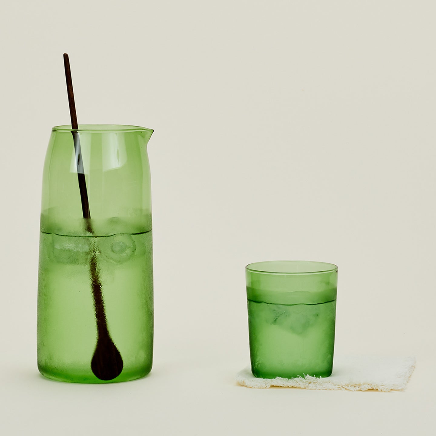 Essential Glassware Pitcher in Green, filled with ice water, along with a drinking glass and stirring spoon.