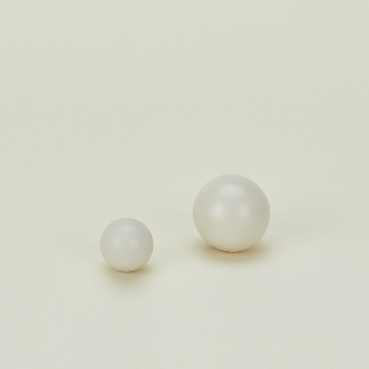 Two white spherical pearls of different sizes placed on a plain light background. The smaller pearl is on the left, and the larger pearl is on the right.