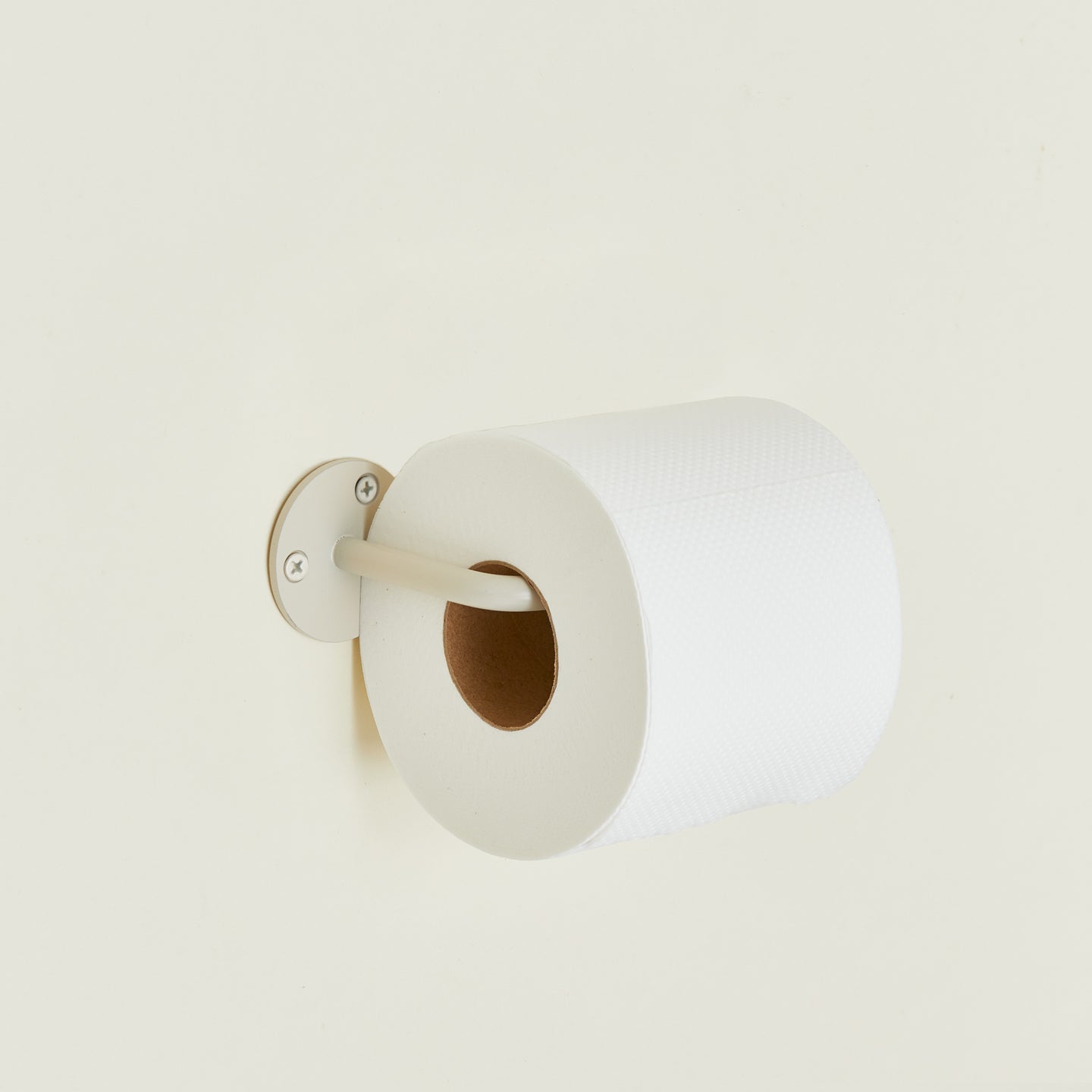 Toilet paper holder in Ivory with a roll of toilet paper.