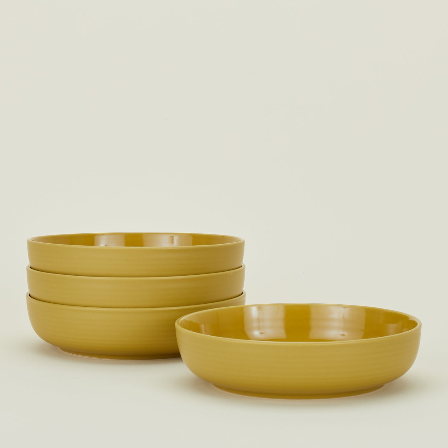 Four mustard yellow Essential Low Bowls.