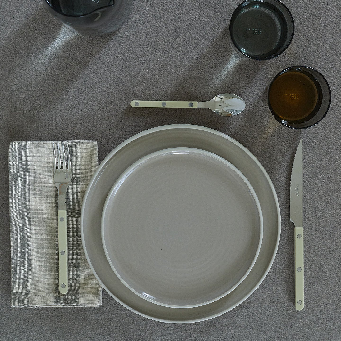 Placesetting with Essential Striped Dinner Napkin in Light Grey and Dark Grey on grey tablecloth.