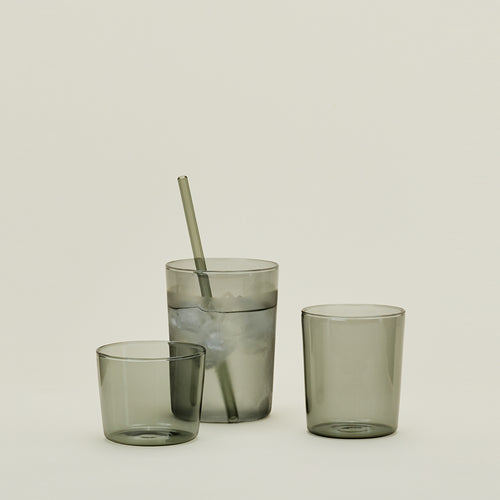 Group of three Essential Glasses in Smoke in various sizes, filled with water and fruit with a coordinating glass straw.